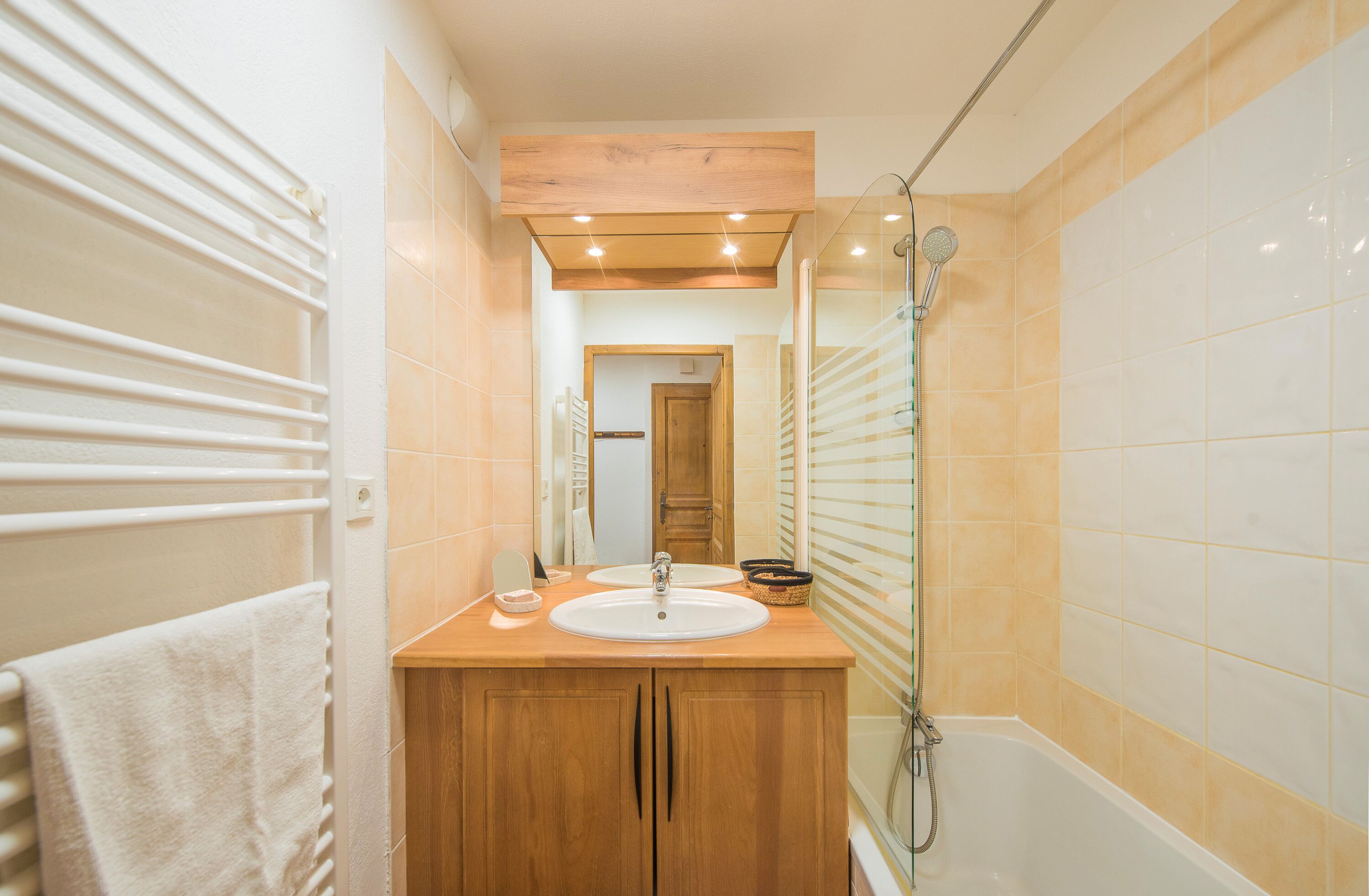 A bathroom with a wooden vanity, two sinks, a mirror, and a shower.