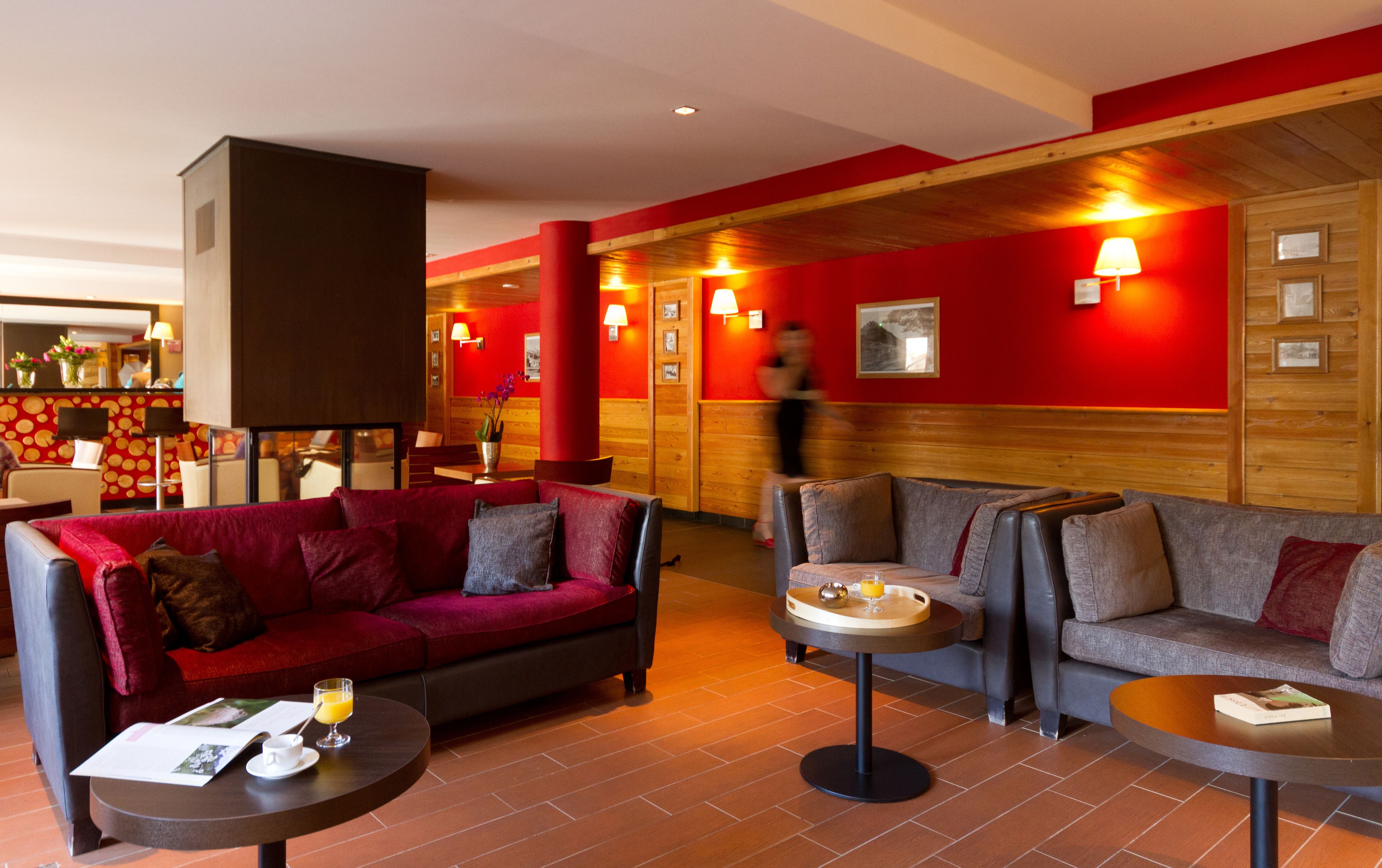 A hotel lobby with red walls, wooden paneling, and a mix of seating areas including sofas and a small table with a tray.