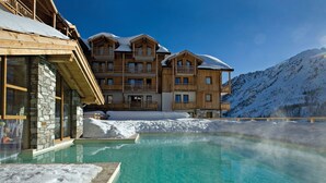Un hotel con piscina rodeado de nieve, balcones de madera y un paisaje de montaña.
