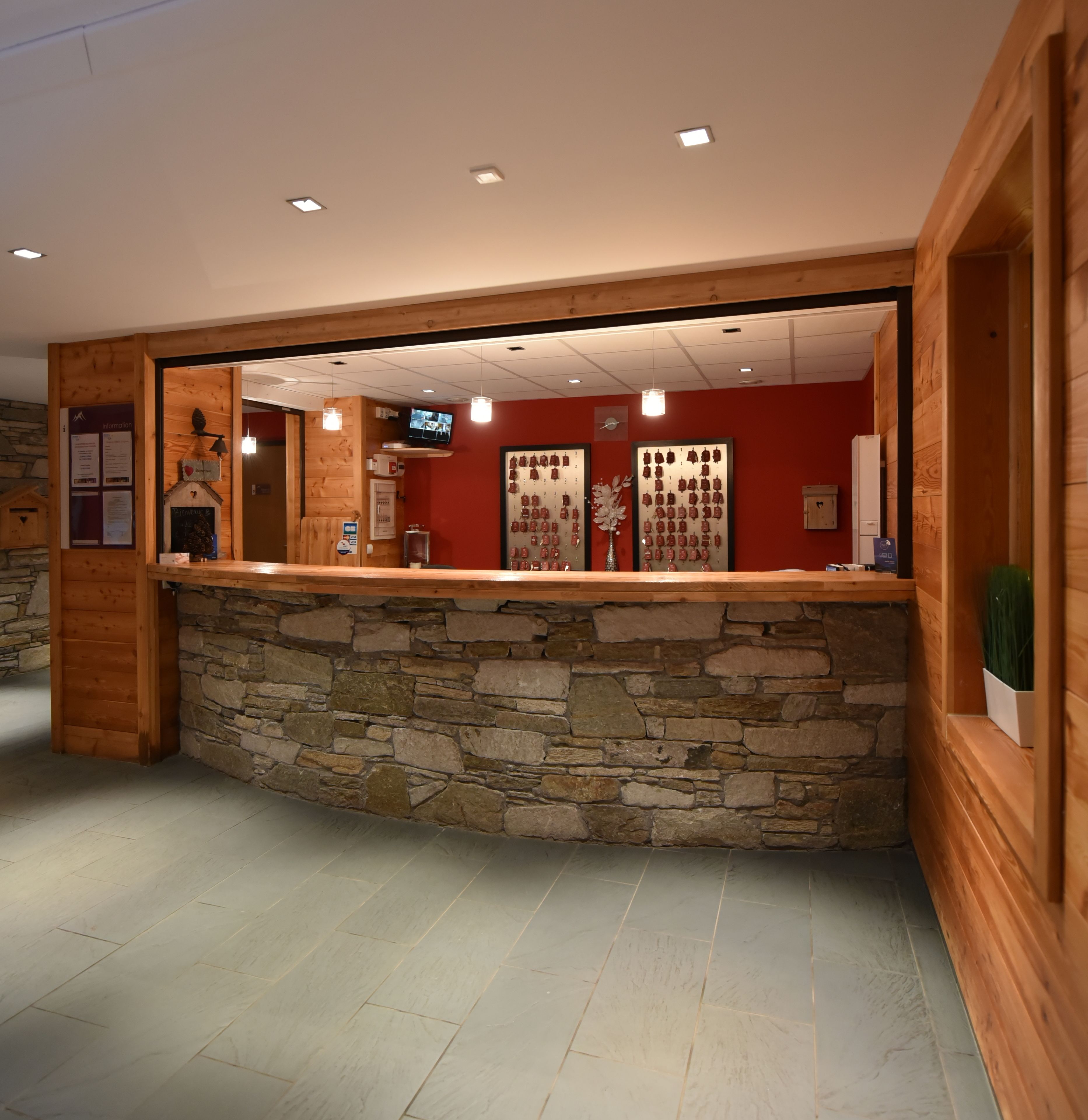 Un espace d’accueil avec un mur en pierre et un lambris en bois, un téléviseur fixé au mur et un comptoir où sont exposés divers objets.