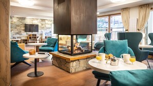 Un espacio interior acogedor con una chimenea de piedra, cómodas sillas color turquesa y una mesa con alimentos para el desayuno.
