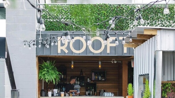Un bar situé sur un toit, avec une enseigne indiquant « TOIT », des places assises en plein air et des plantes en pot.