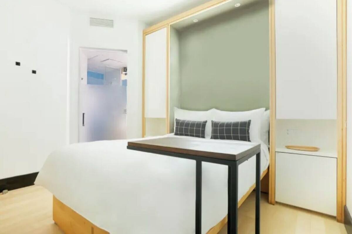 Una habitación de hotel moderna con cama, mesita de noche y un pequeño armario.