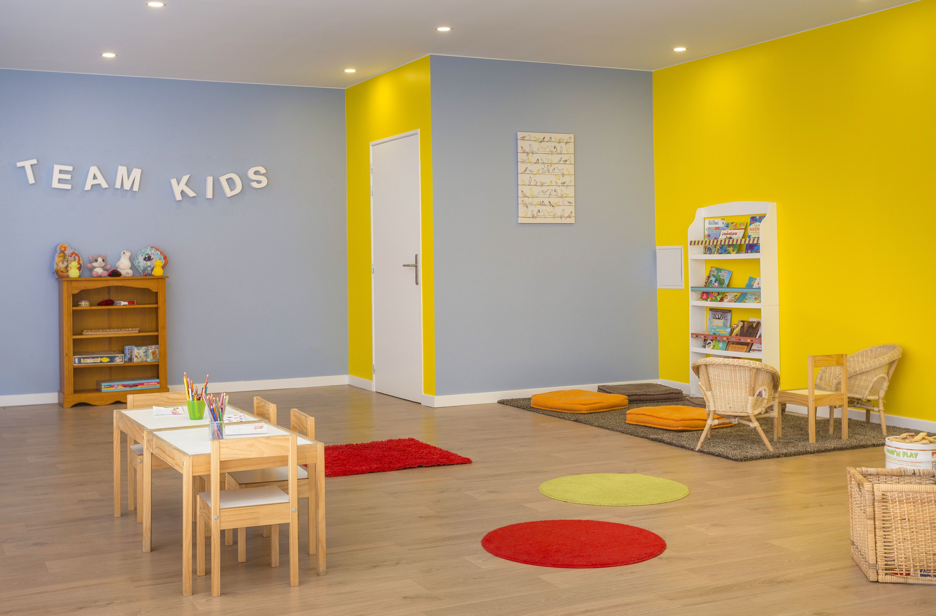 A children's playroom with a table, chairs, a bookshelf, and a colorful wall.