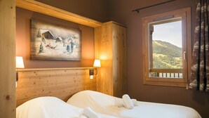 Quarto de hotel com duas camas, um quadro representando uma paisagem nevada, uma janela com vista para uma montanha arborizada e uma cabeceira de madeira.