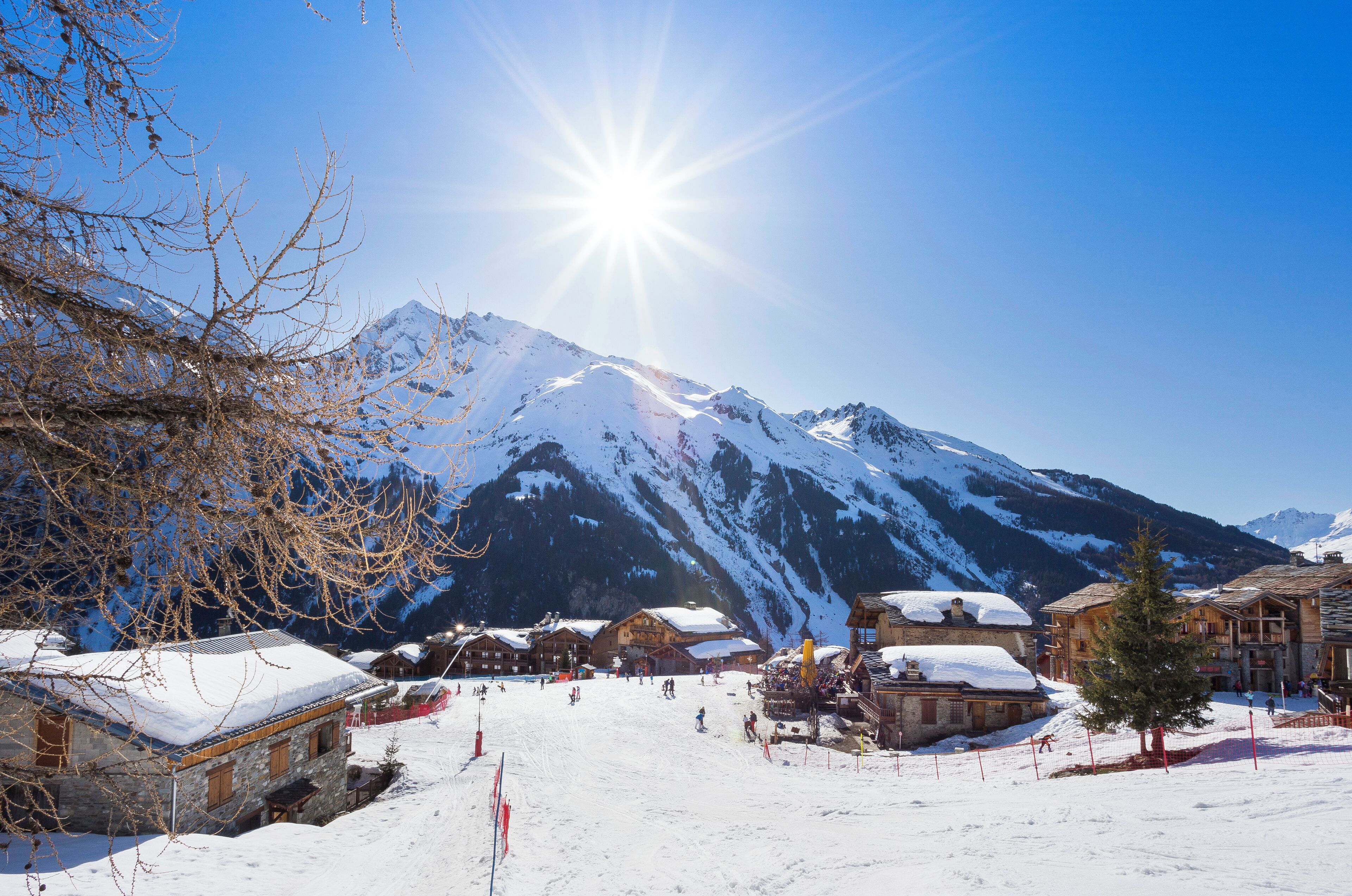 A snow-covered mountain village with wooden buildings, a ski slope, and a clear blue sky.