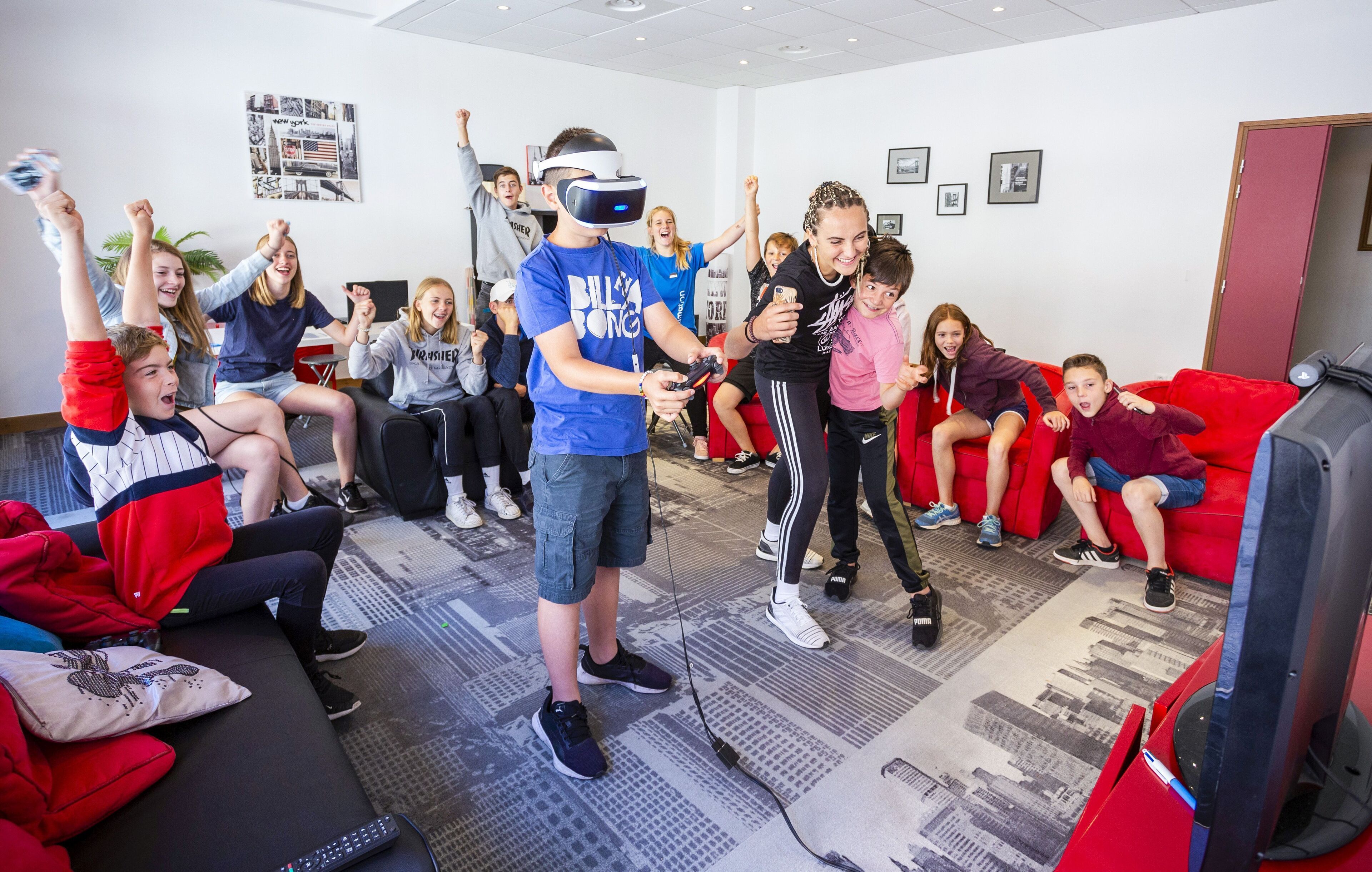 A group of people in a room with a VR headset, a red couch, and a carpet with a cityscape design.