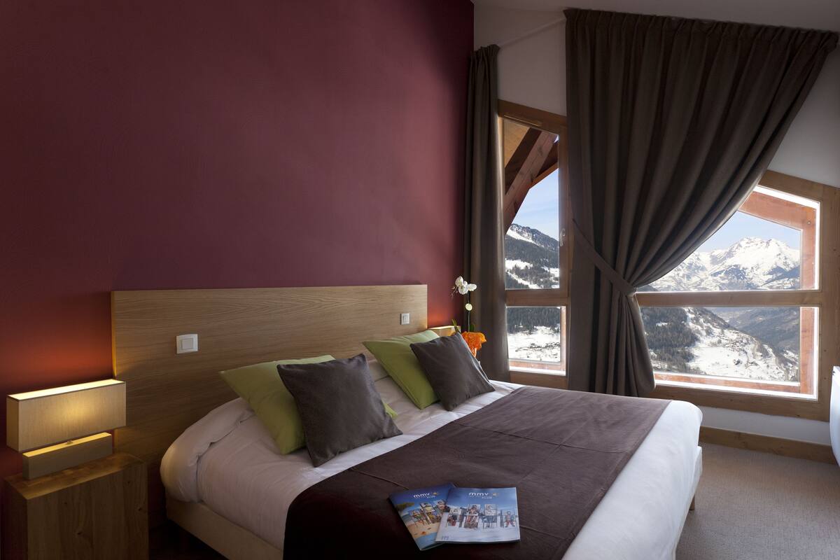 A bedroom with a large bed, wooden headboard, and a view of snow-capped mountains through a window.