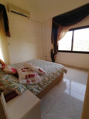 A bedroom with a bed, a window with curtains, a radiator, and a tiled floor.
