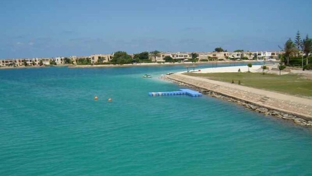 Une vue sur la côte, avec une eau turquoise et limpide, une plage de sable et une rangée de bâtiments le long du rivage.