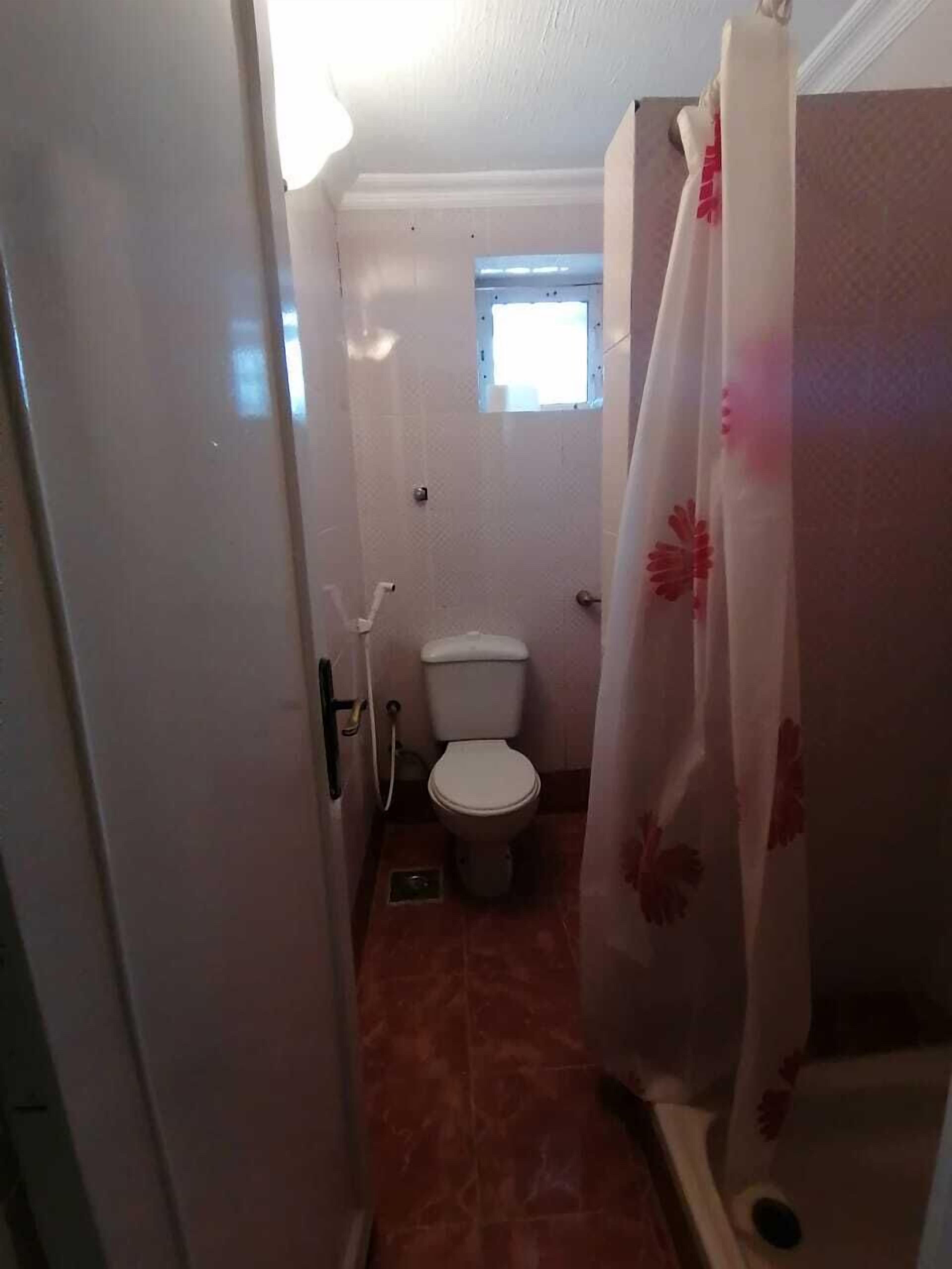Een kleine badkamer met toilet, douche en een raam.