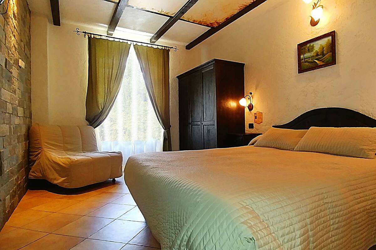 A bedroom with a bed, a nightstand, a wardrobe, and a window with curtains.