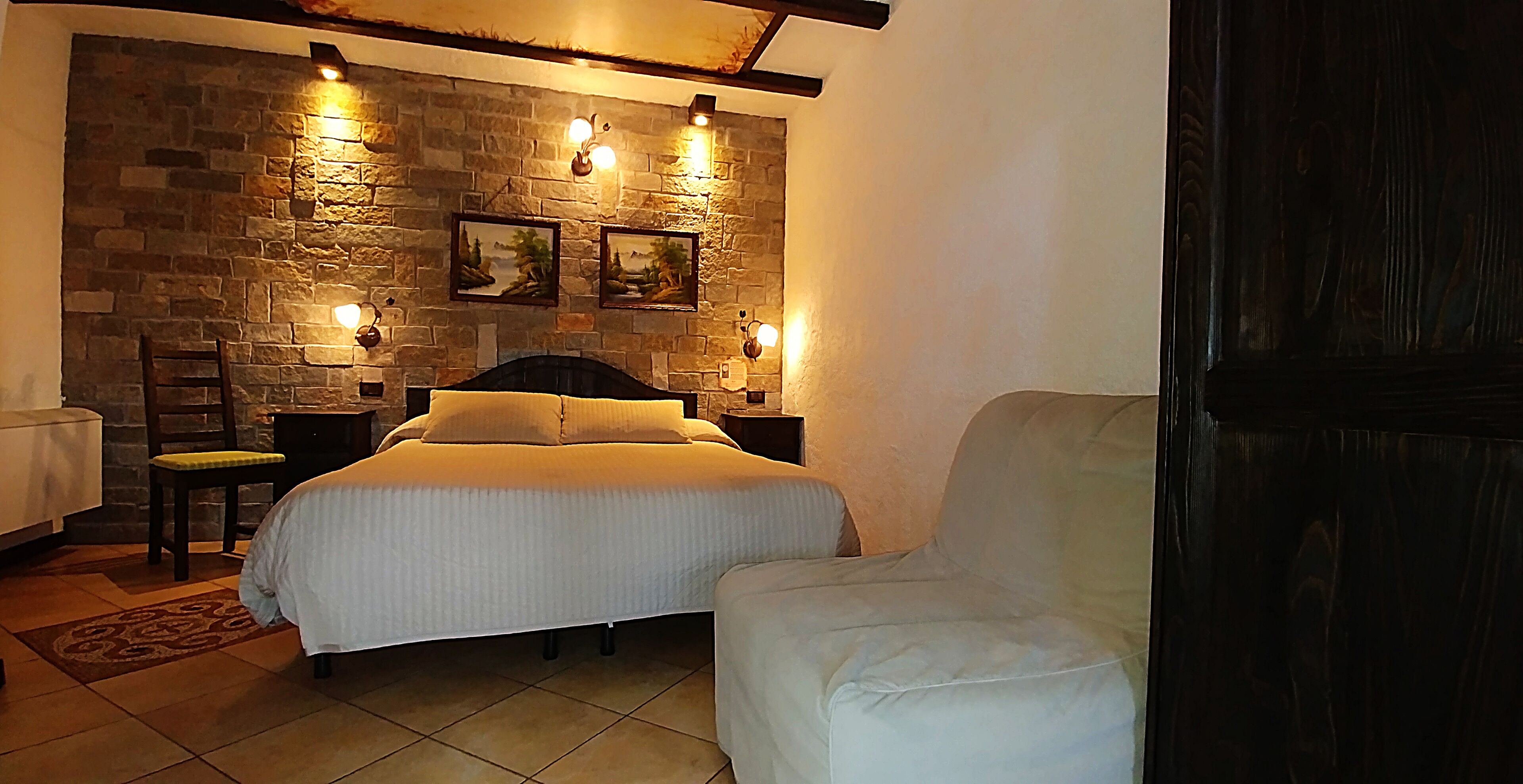 A bedroom with a bed, a chair, a stone wall, and two wall-mounted lights.