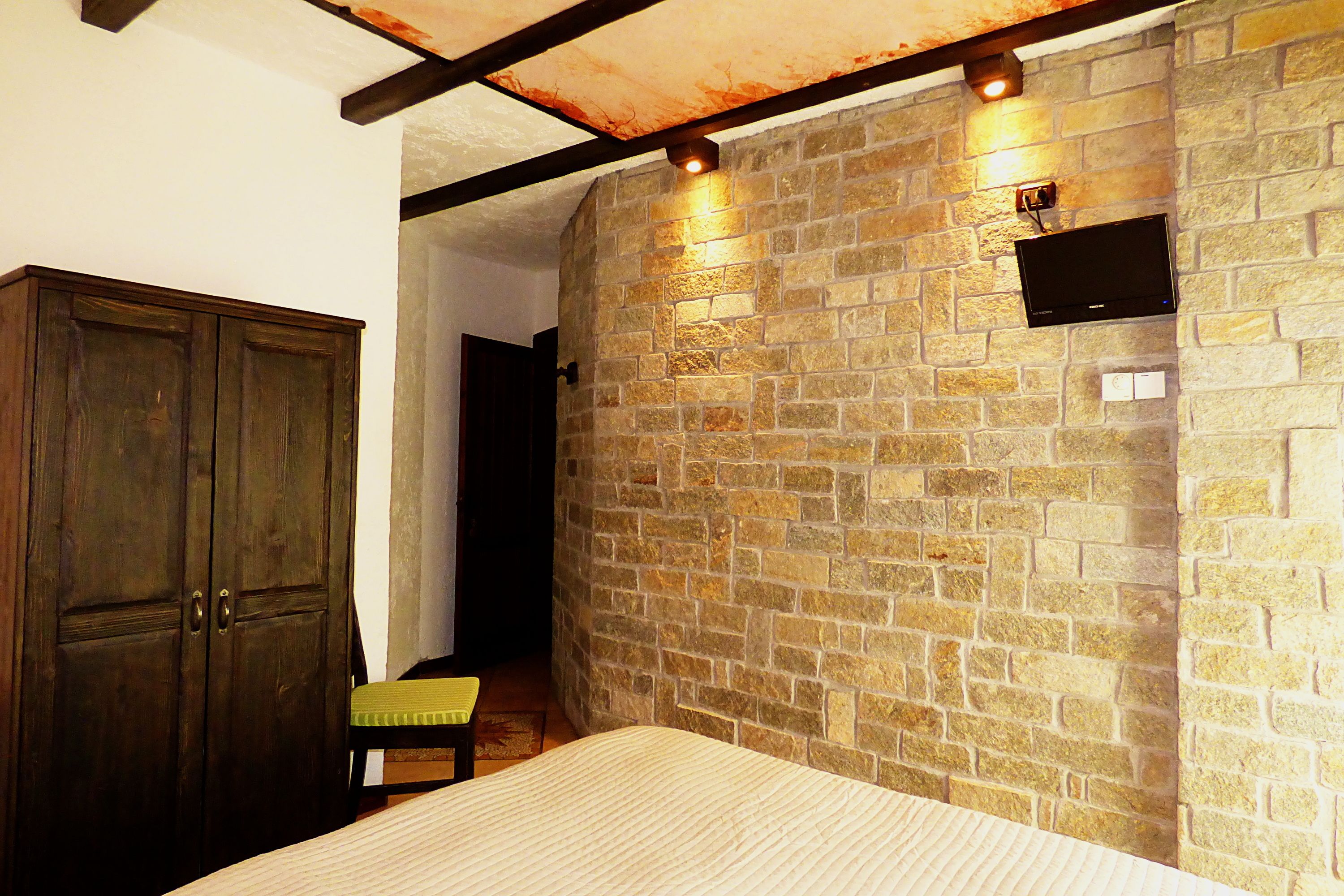 Un dormitorio con pared de piedra, armario de madera y cama con cojín verde.