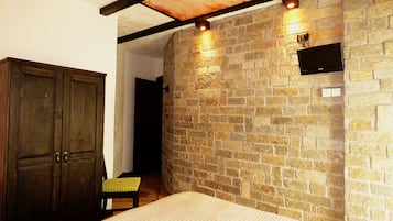 Un dormitorio con pared de piedra, armario de madera y cama con cojín verde.