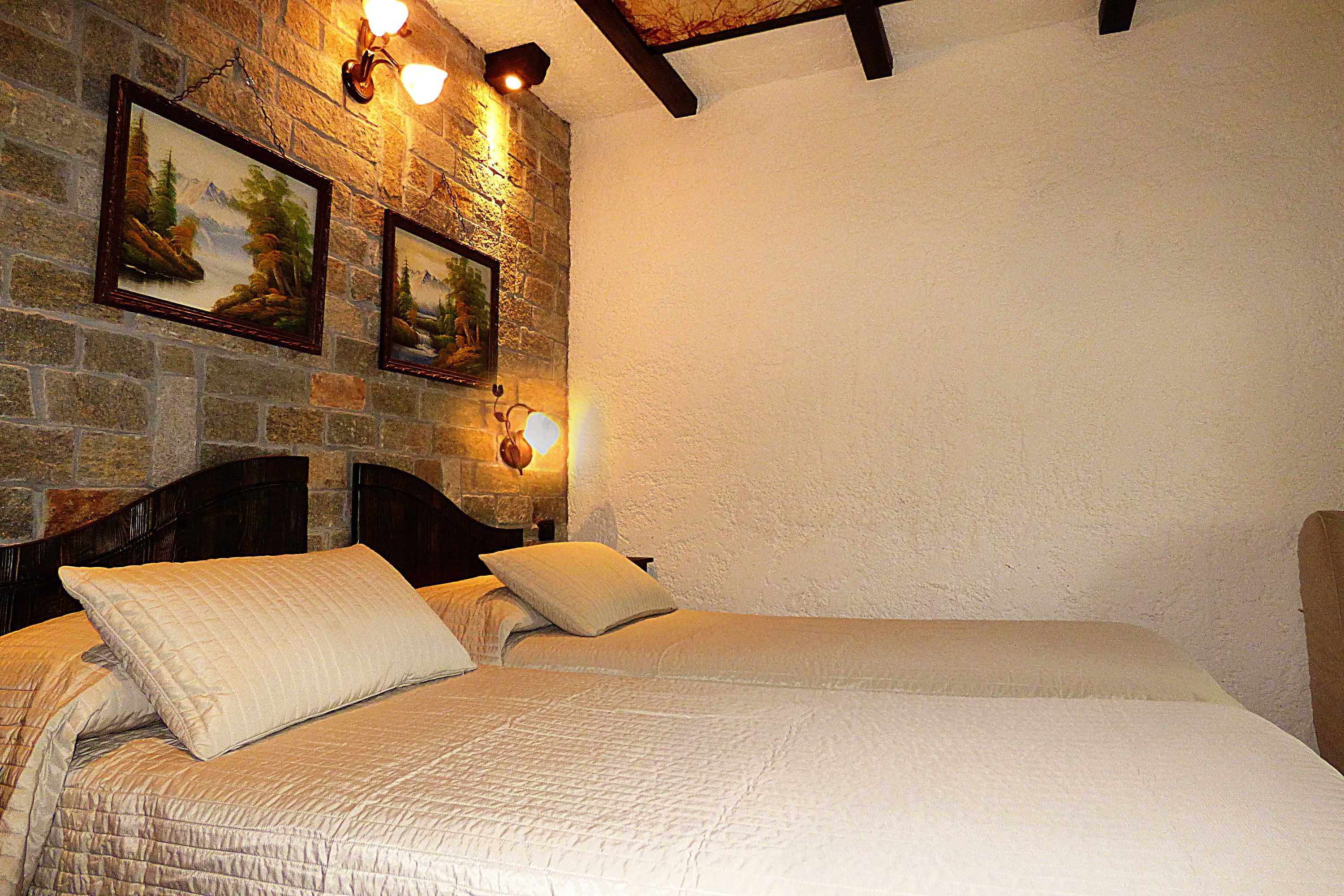 Une chambre avec un mur en pierre, une tête de lit en bois et deux tableaux encadrés.