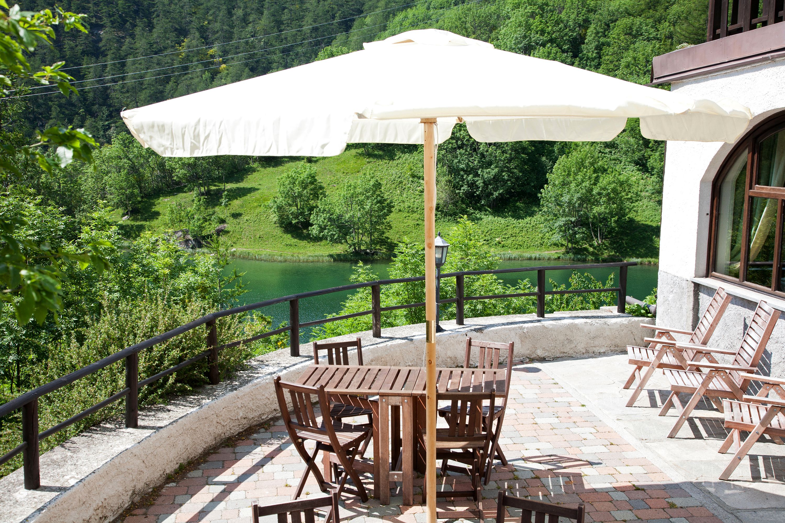 Una terraza con mesa y sillas, un paraguas blanco y vistas a un valle verde.