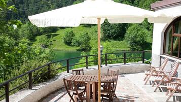 Una terraza con mesa y sillas, un paraguas blanco y vistas a un valle verde.