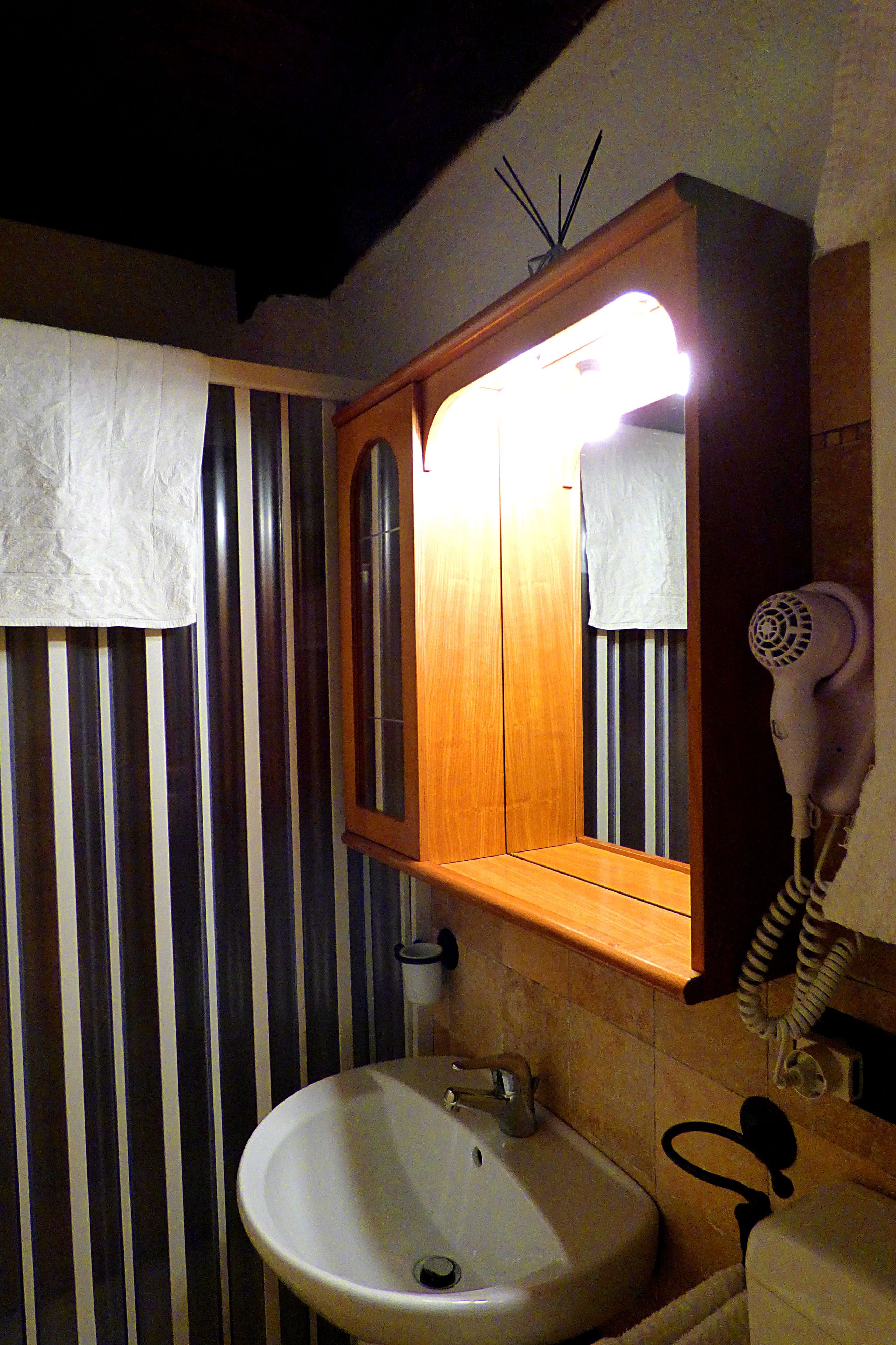 A bathroom with a wooden vanity, a white sink, a mirror, and a hairdryer on the wall.