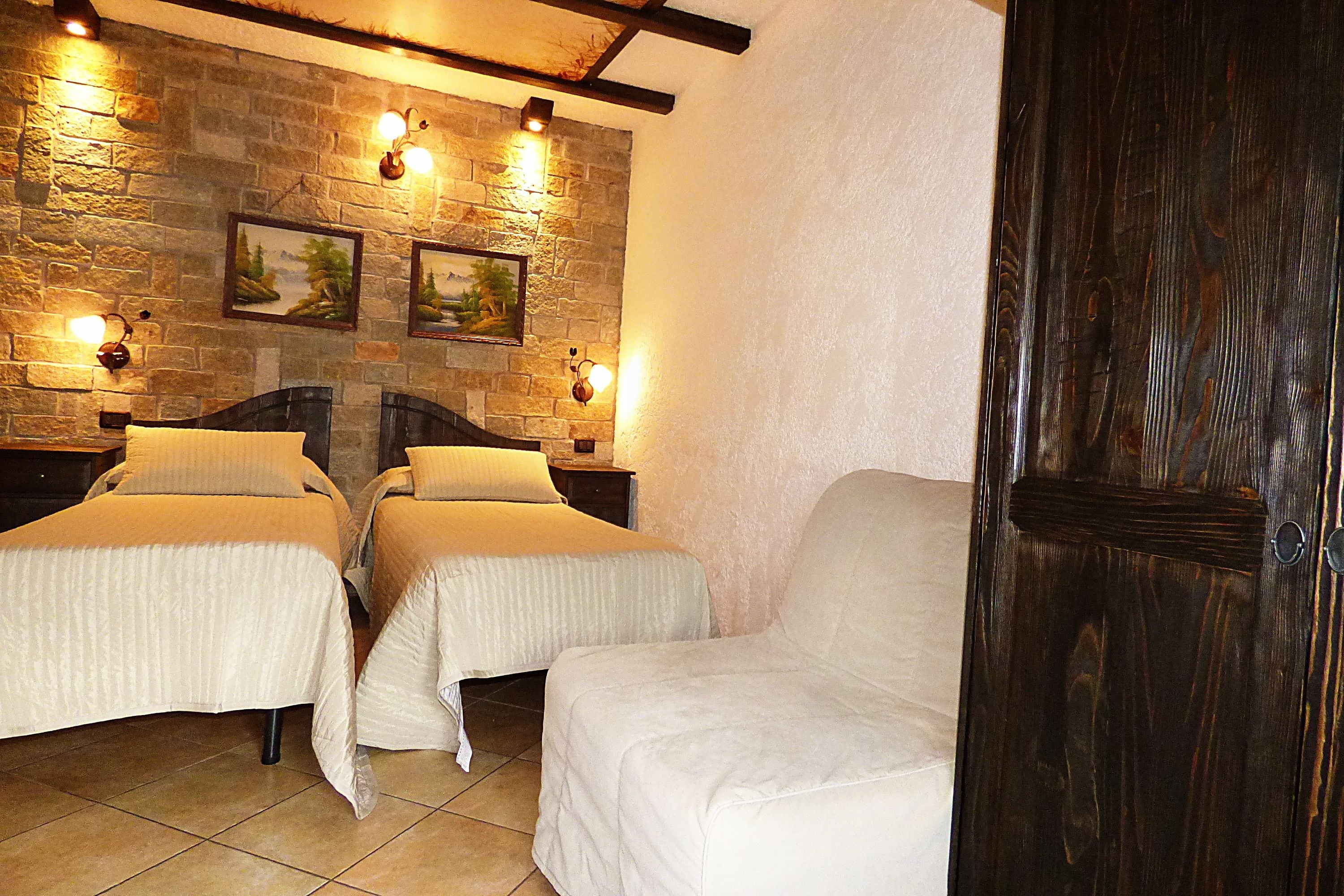 A room with two beds, a wooden door, stone walls, and wall-mounted lights.
