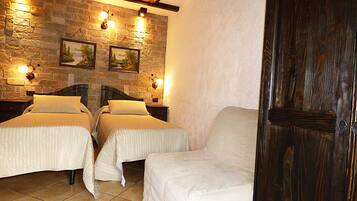 A room with two beds, a wooden door, stone walls, and wall-mounted lights.