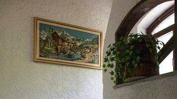 A staircase with stone steps and a wooden handrail, leading to a landing with a framed painting of a mountainous landscape and a hanging plant.