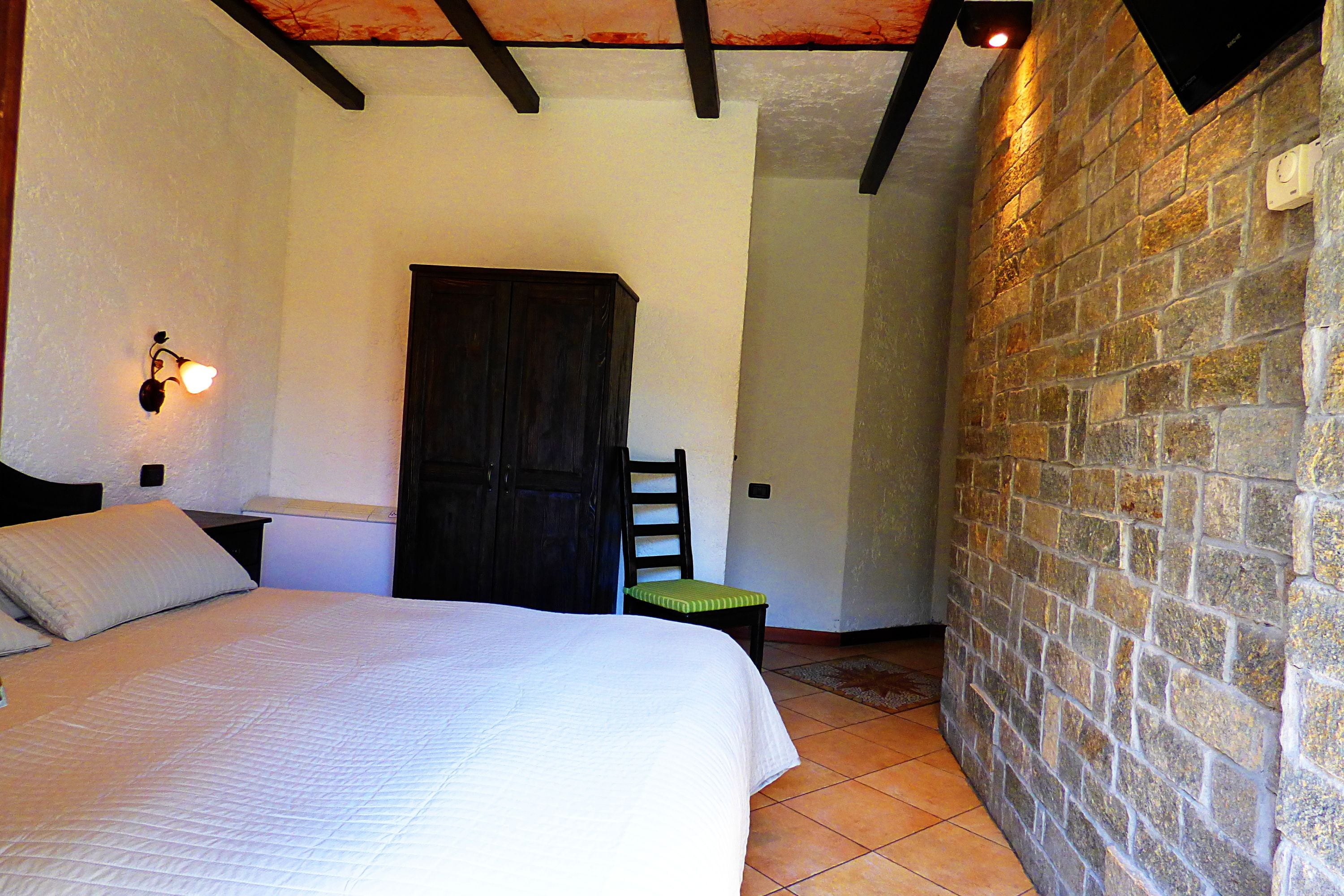 Un dormitorio con cama, una silla, una mesita de noche, una lámpara de pared y una puerta.