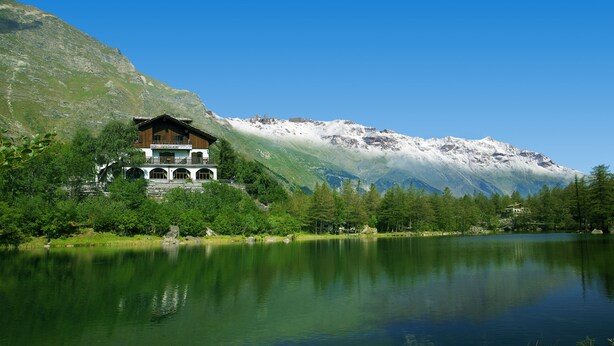 A chalet with a balcony overlooking a lake, surrounded by mountains and greenery. - Chalet sul lago Hotel In Montagna (Moncenisio)