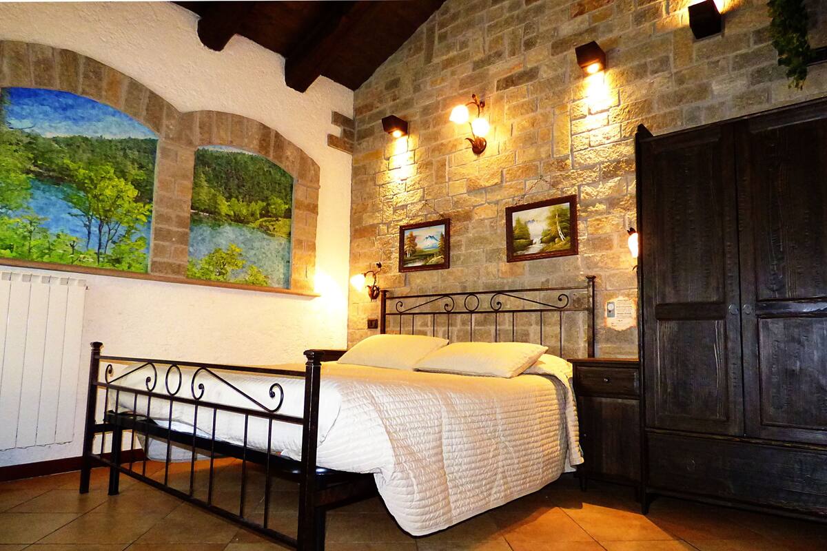 A bedroom with a bed, stone walls, and a mural of a landscape.