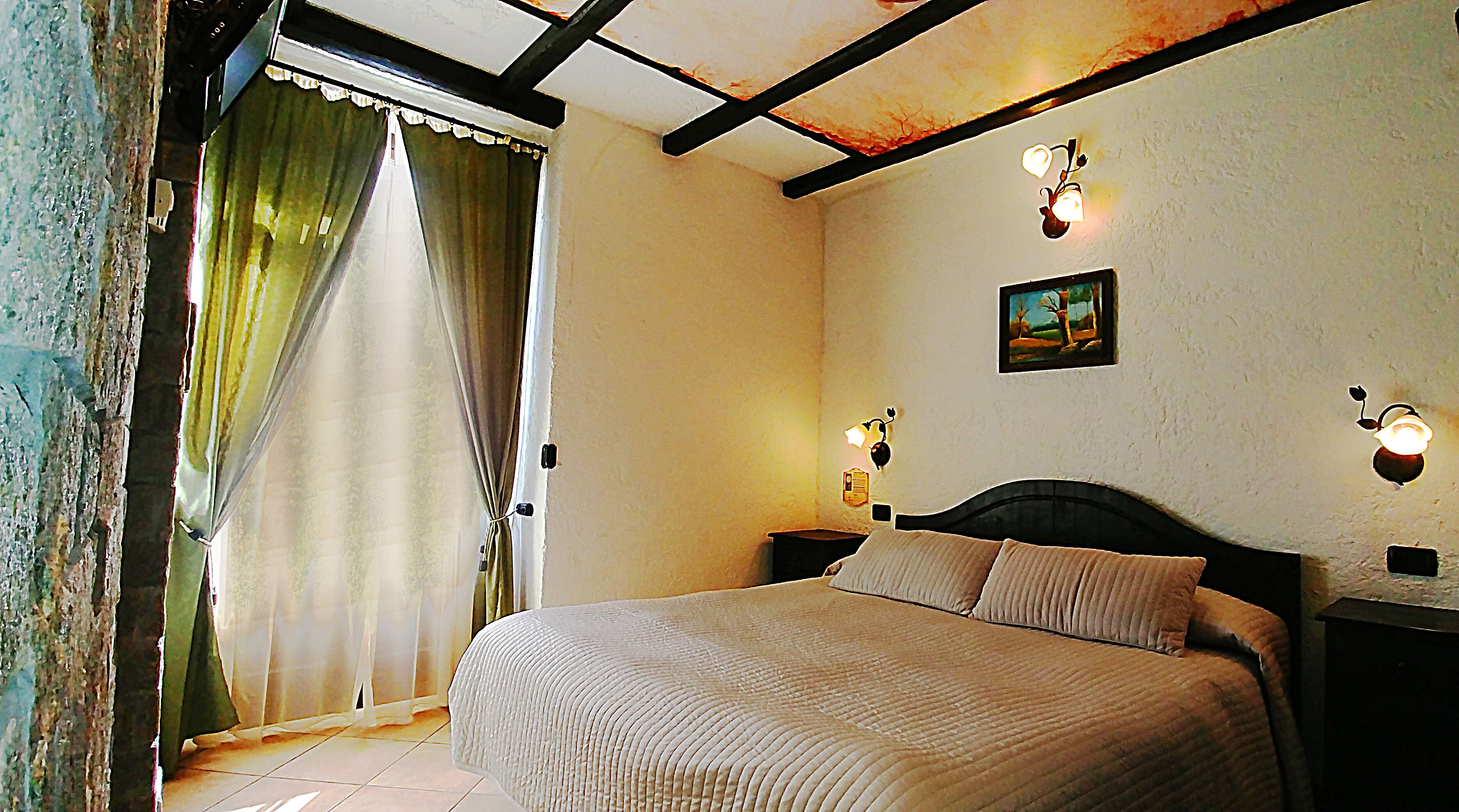 Quarto com cama, cortinas e luminárias fixadas na parede.