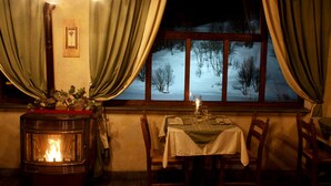 A cozy room with a wood-burning stove, a table set for dining, and a window with curtains. - Chalet sul lago Hotel In Montagna (Moncenisio)