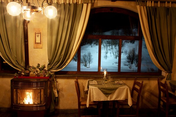 Una habitación acogedora con una estufa de leña, una mesa lista para cenar y un ventanal con cortinas.