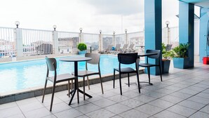 A rooftop pool area with lounge chairs and tables, surrounded by a white fence and city views. - Hôtel Bano Palace (Douala)