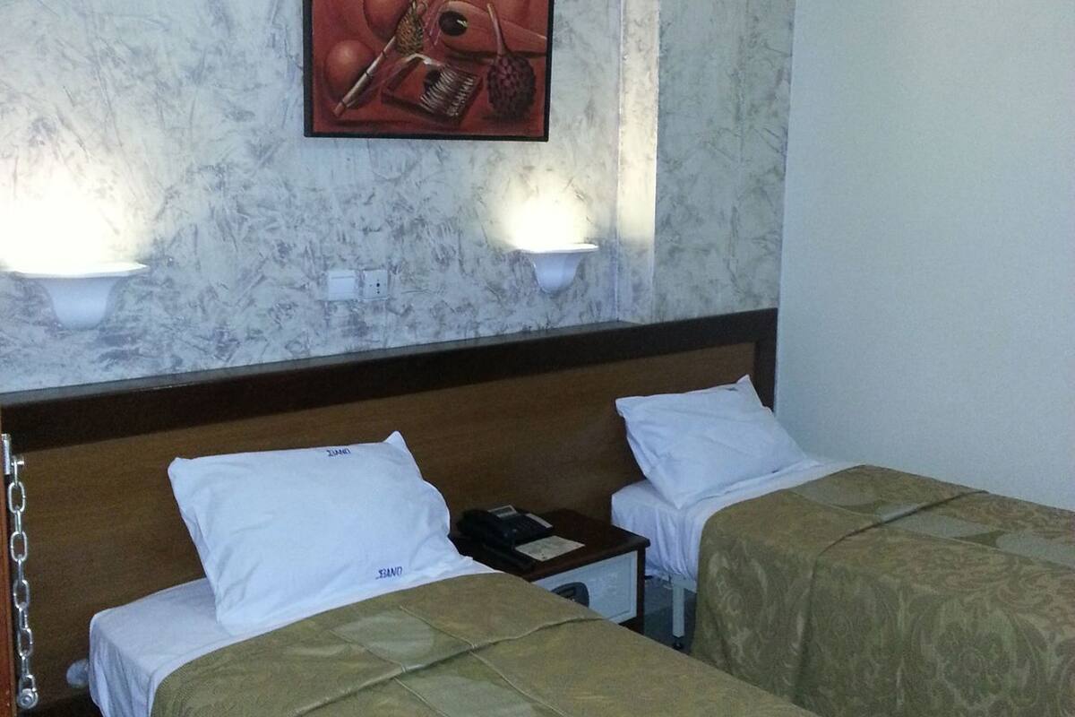 A hotel room with two beds, a marble wall, a painting, and two wall-mounted lamps.