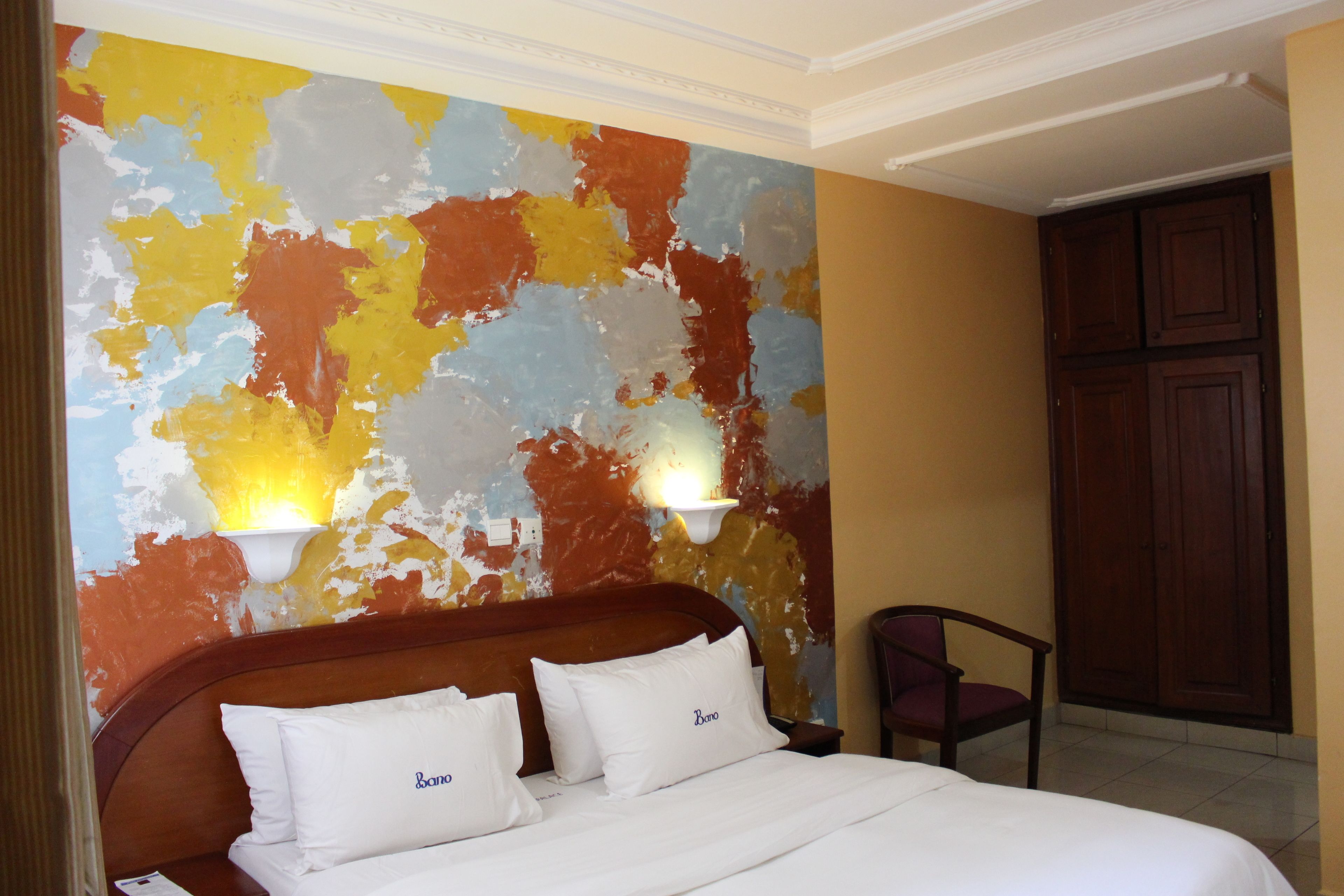 Une chambre d’hôtel avec un lit, deux lampes fixées au mur et une armoire en bois.