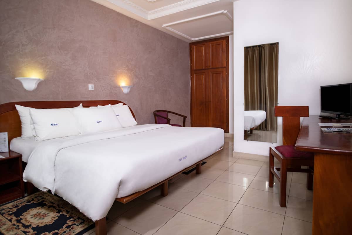A hotel room with a bed, a desk, a chair, a TV, and a wardrobe.