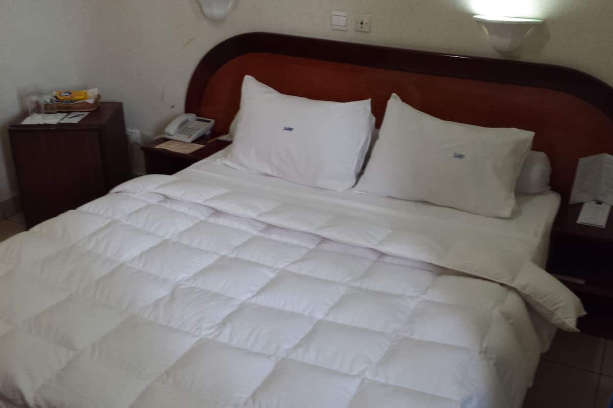 A neatly made bed with a white quilt and pillows, a bedside telephone, and a nightstand with a lamp.