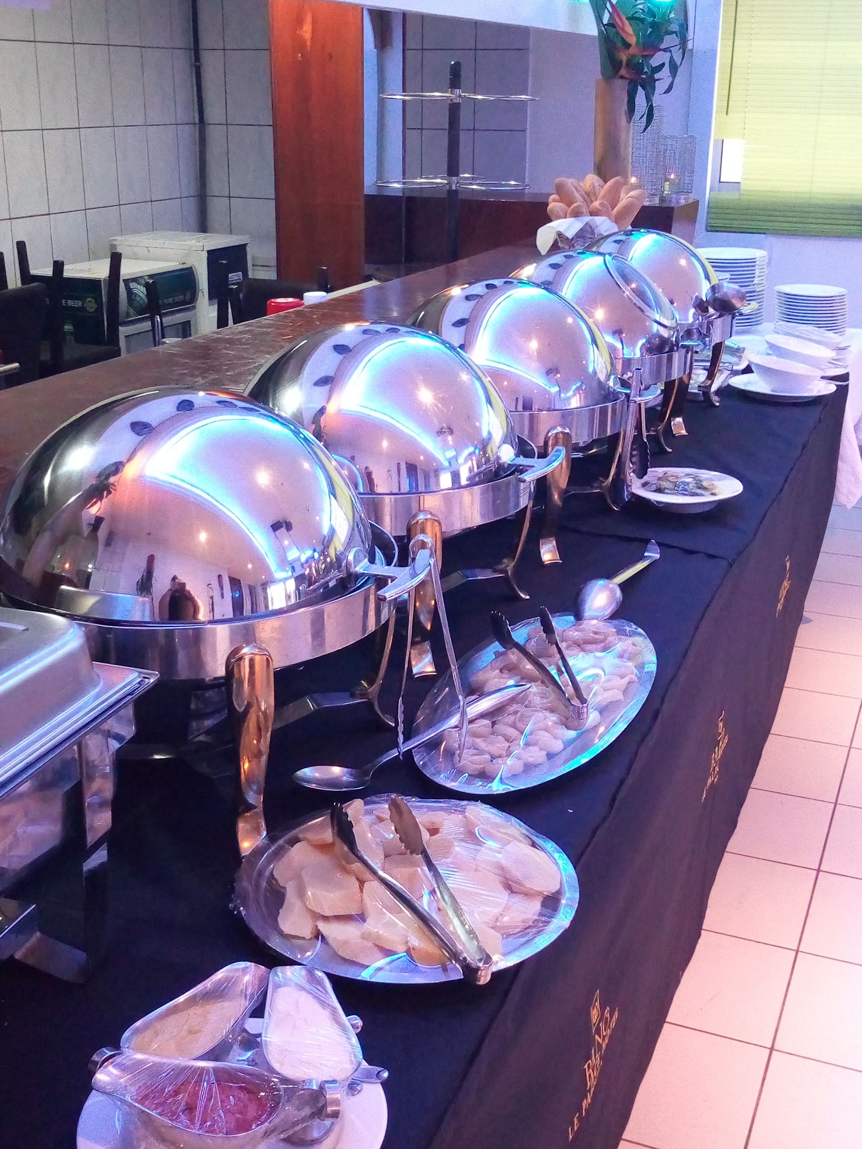 A buffet setup with multiple covered food stations, including a variety of dishes and utensils.