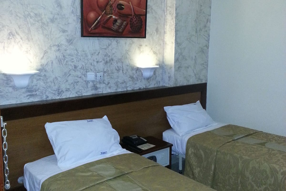 A hotel room with two beds, a marble wall, a painting, and an air conditioning unit.