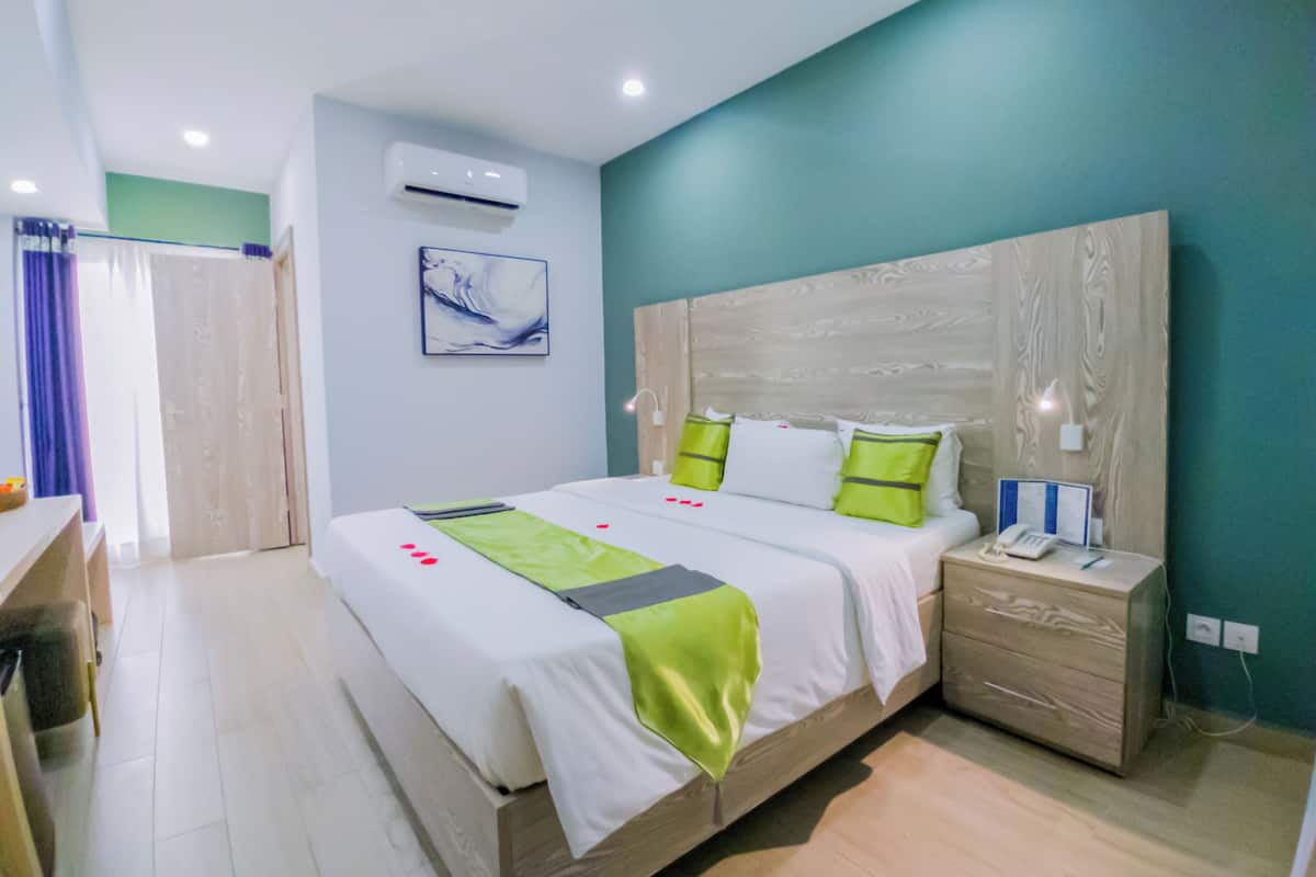 A modern hotel room with a large bed, bedside table, and a wall-mounted air conditioner.