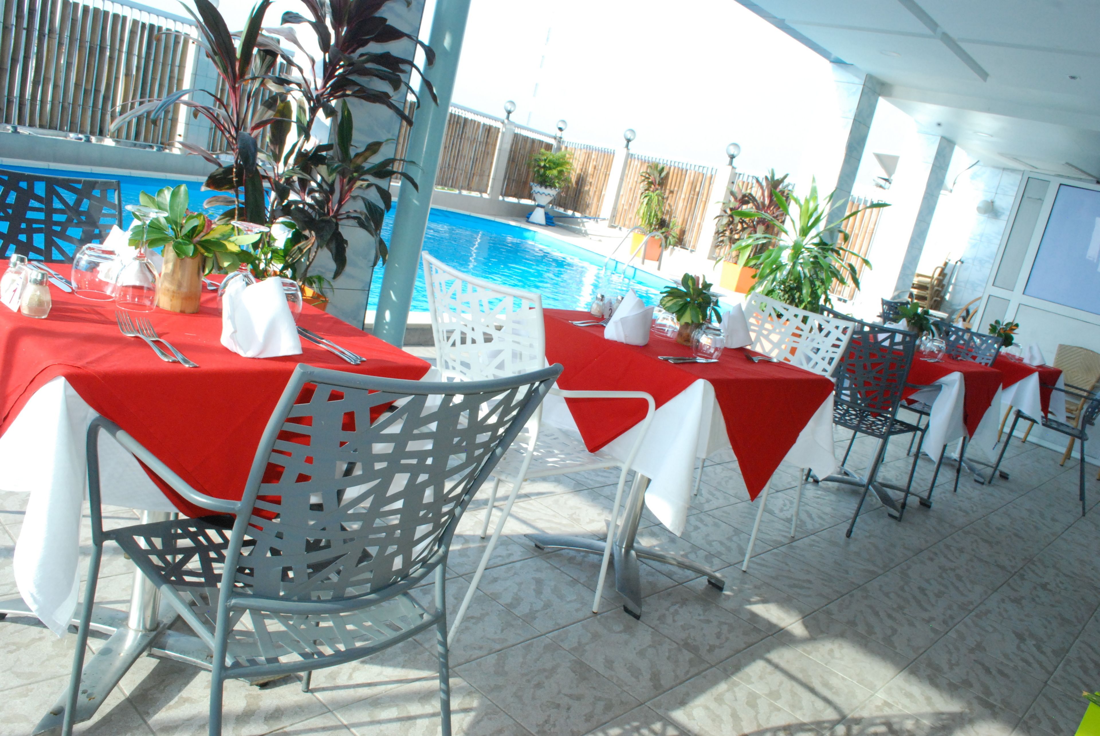 Un espace repas aménagé au bord de la piscine, avec des tables pour deux, entouré de plantes en pot et donnant sur la piscine.