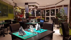 A restaurant with tables set for dining, chairs, and potted plants. - Hôtel Bano Palace (Douala)