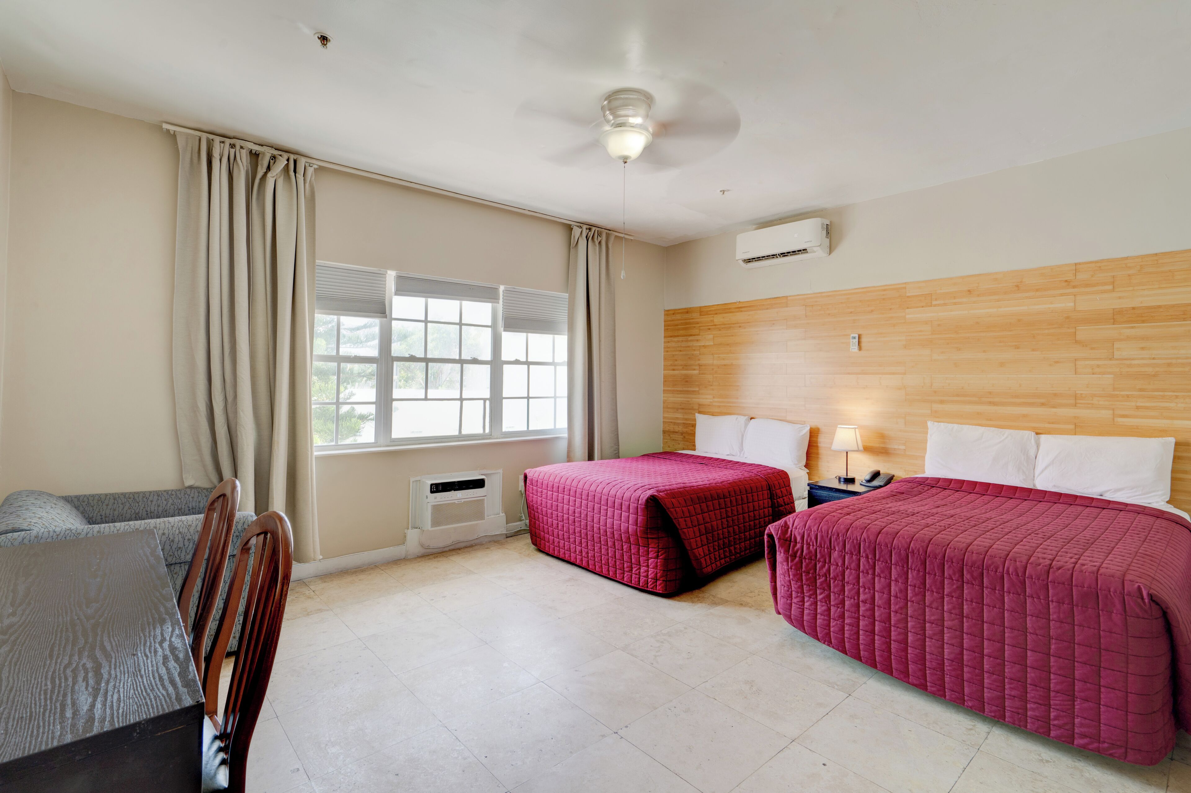 A hotel room with two beds, a sofa, a desk, and a window with curtains.