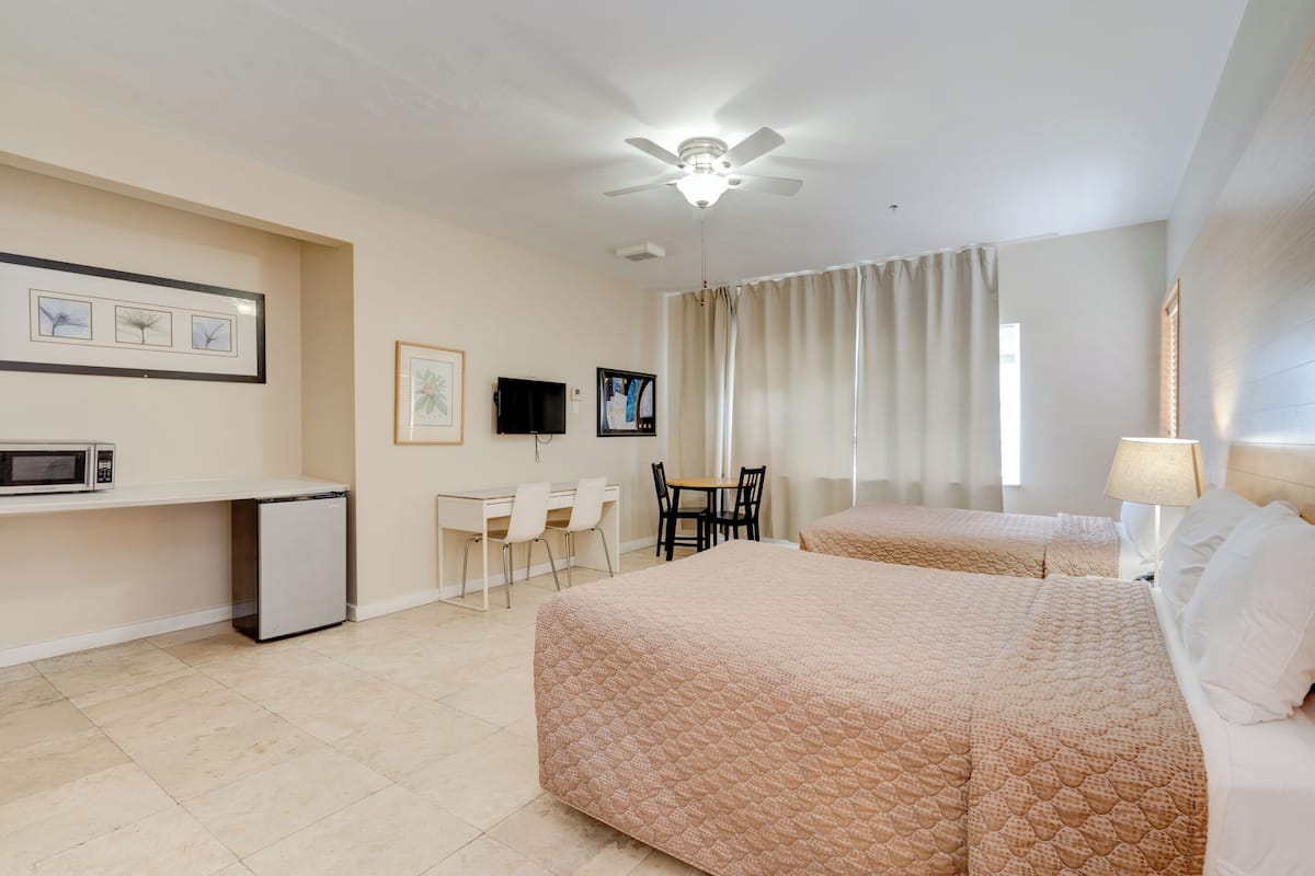 A hotel room with two beds, a desk with a chair, a TV, and a ceiling fan.