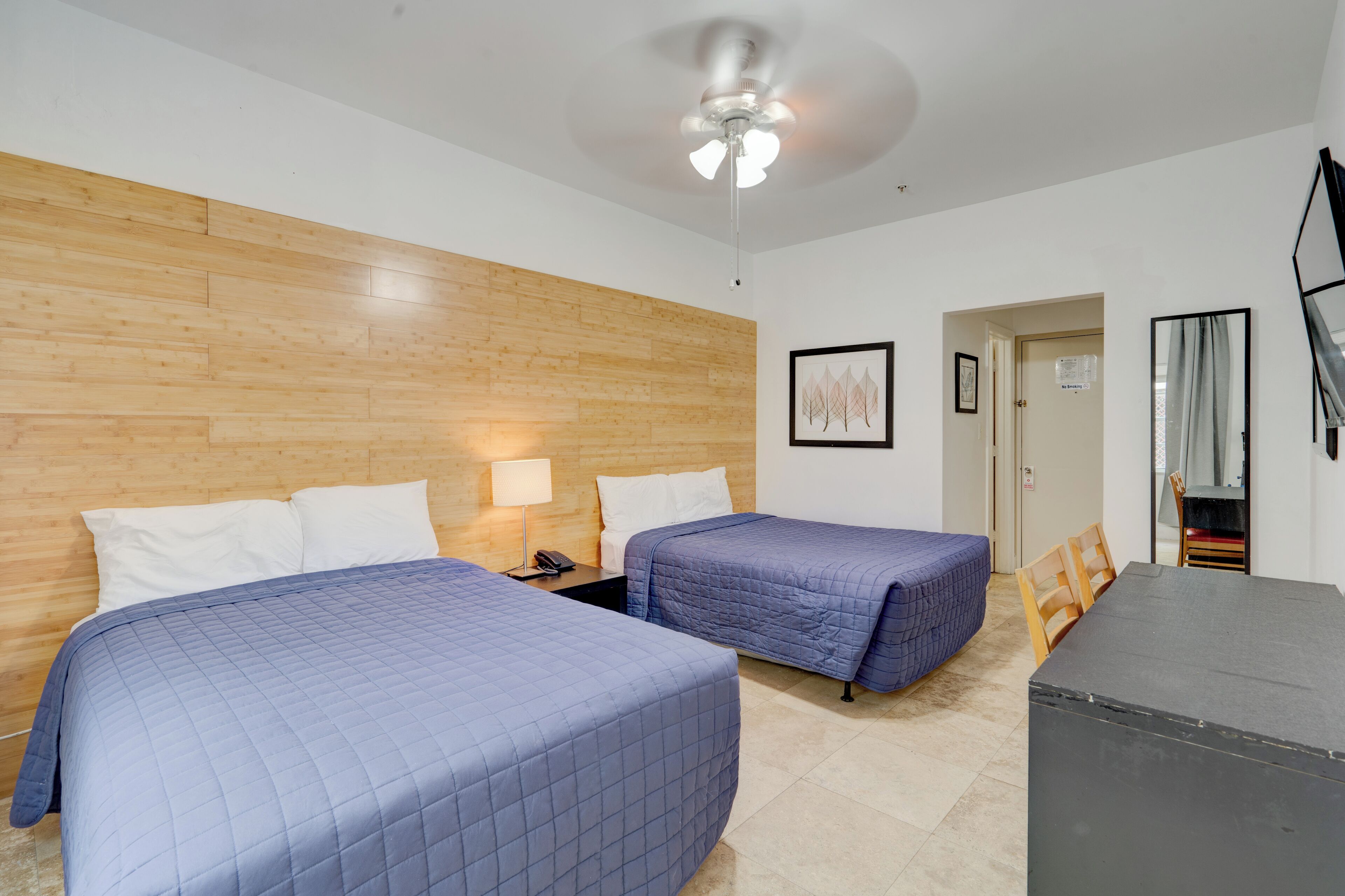 Een hotelkamer met twee bedden, een plafondventilator, een bureau en een stoel.