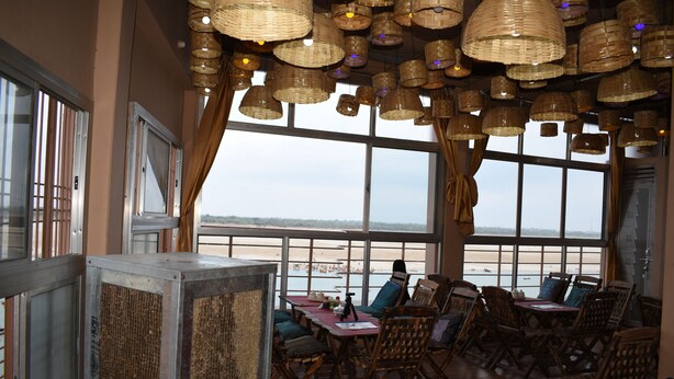 A restaurant with large windows, wicker ceiling lamps, and wooden furniture. - Shri Guest House (Varanasi)
