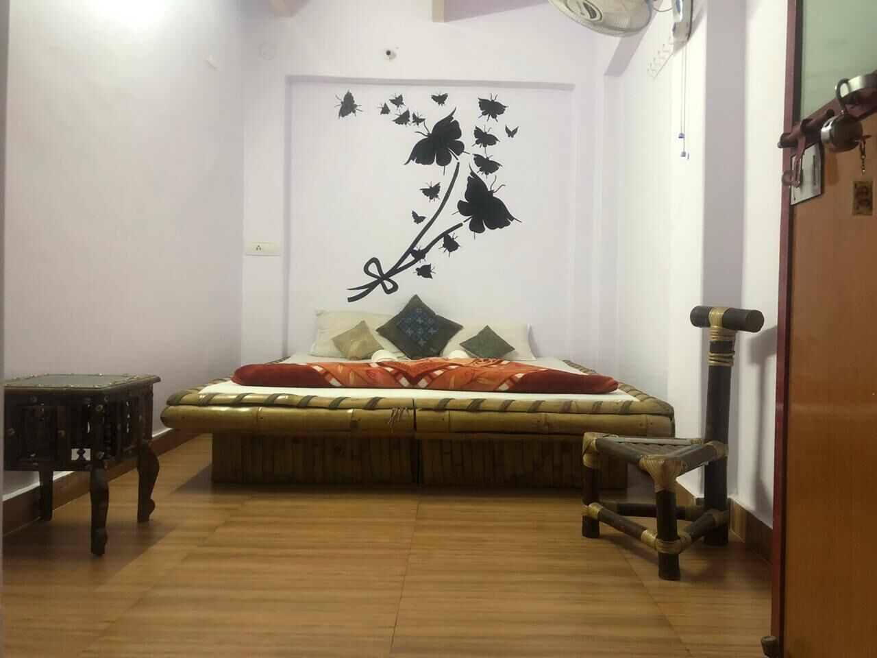 A bedroom with a bed, a wall-mounted fan, a wooden floor, and a cat tree.