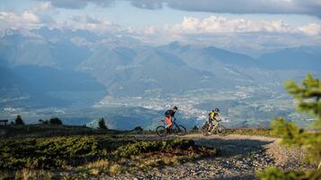 Dos ciclistas en un sendero de montaña con vistas panorámicas de montañas distantes y un valle.