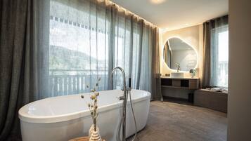 Un baño moderno con una bañera independiente, un tocador con espejo y un ventanal con cortinas.