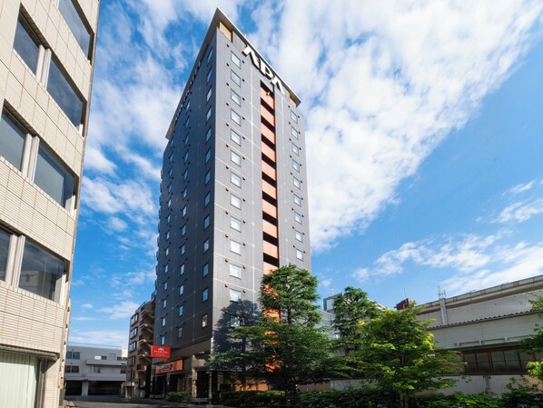 Un grand immeuble abritant un hôtel, avec de nombreux étages, une enseigne indiquant qu’il s’agit d’un hôtel, et un ciel dégagé avec quelques nuages.